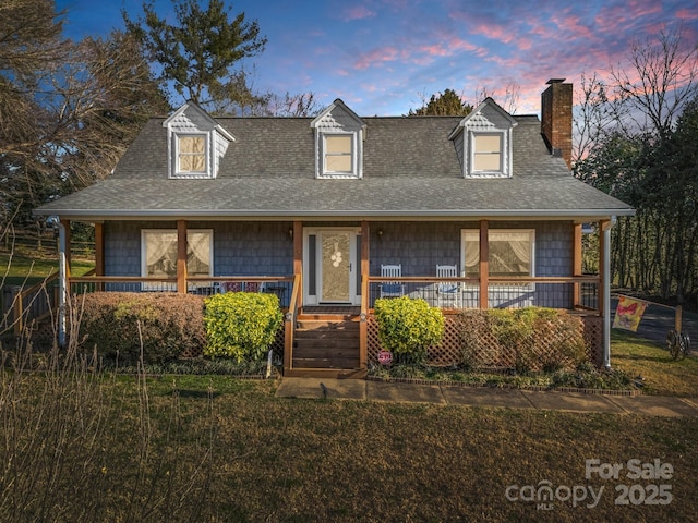 view of front of home featuring a porch, a chimney, a yard, and a shingled roof