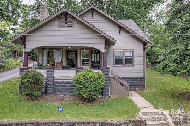 bungalow-style house with roof with shingles, a porch, a chimney, and a front yard