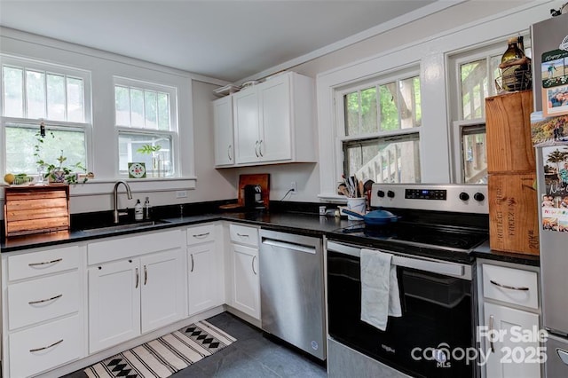 kitchen with appliances with stainless steel finishes, dark countertops, a sink, and white cabinetry