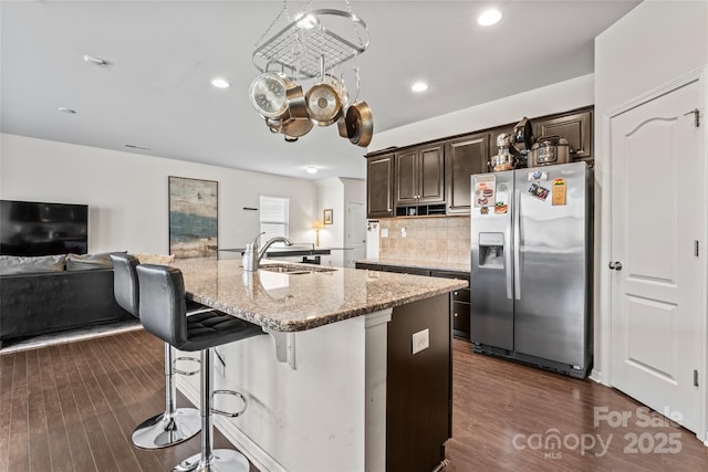 kitchen with a breakfast bar, a sink, stainless steel fridge with ice dispenser, dark brown cabinets, and light stone countertops