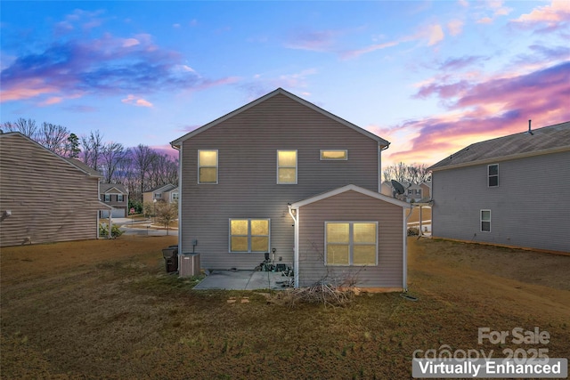 back of property at dusk featuring a yard, a patio, and central air condition unit