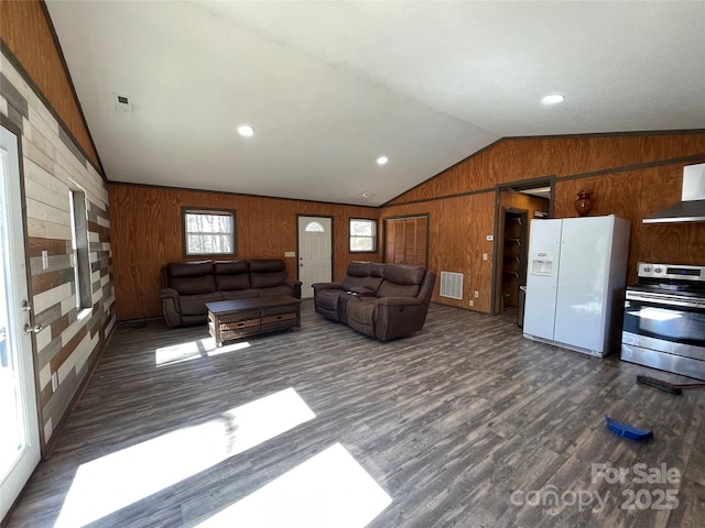 unfurnished living room featuring lofted ceiling, wood walls, dark wood-style floors, and visible vents