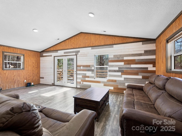 living room with lofted ceiling, wooden walls, a textured ceiling, and wood finished floors