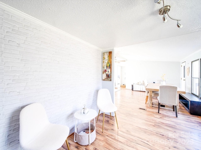 interior space featuring crown molding, brick wall, light wood finished floors, and a textured ceiling