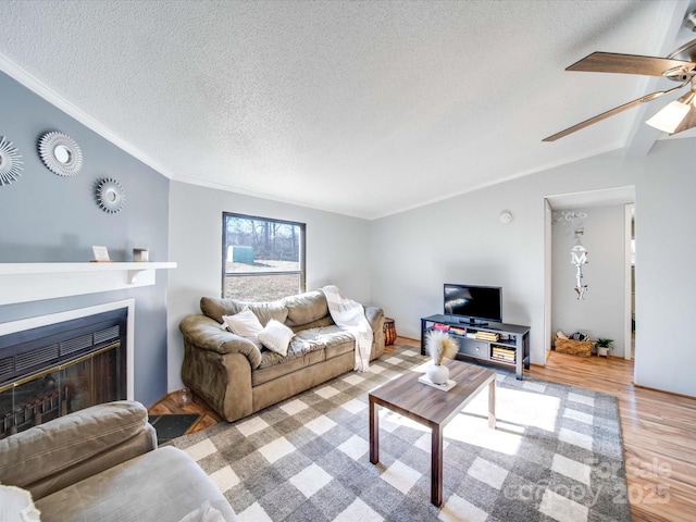 living area with a textured ceiling, wood finished floors, crown molding, ceiling fan, and vaulted ceiling