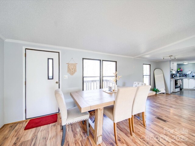 dining space featuring visible vents, crown molding, rail lighting, light wood-style floors, and a textured ceiling