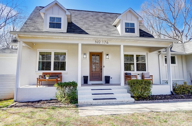 view of front facade featuring brick siding, covered porch, and roof with shingles