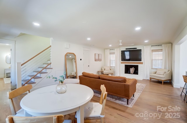 dining space featuring recessed lighting, light wood-style floors, a brick fireplace, ceiling fan, and stairs