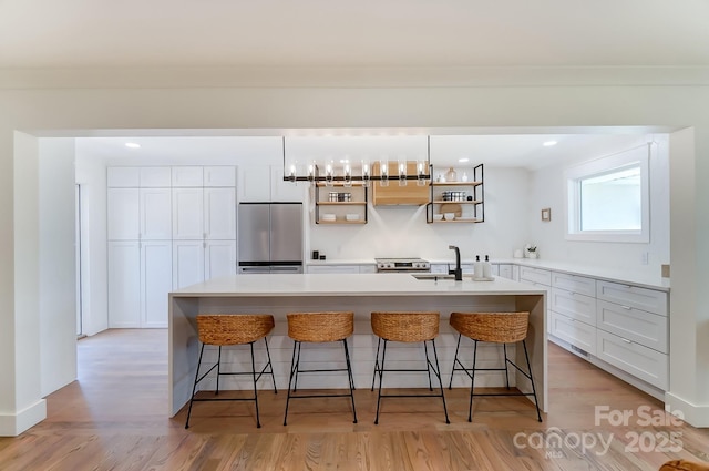 kitchen with a breakfast bar area, white cabinetry, stainless steel appliances, and an island with sink