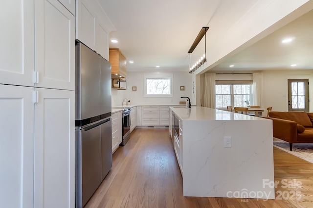 kitchen with a sink, open floor plan, stainless steel appliances, light wood-style floors, and white cabinets