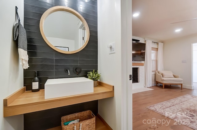 bathroom with a fireplace, recessed lighting, wood finished floors, and a sink