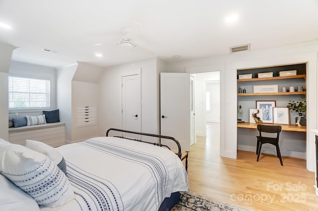 bedroom with visible vents, light wood-style flooring, and built in study area