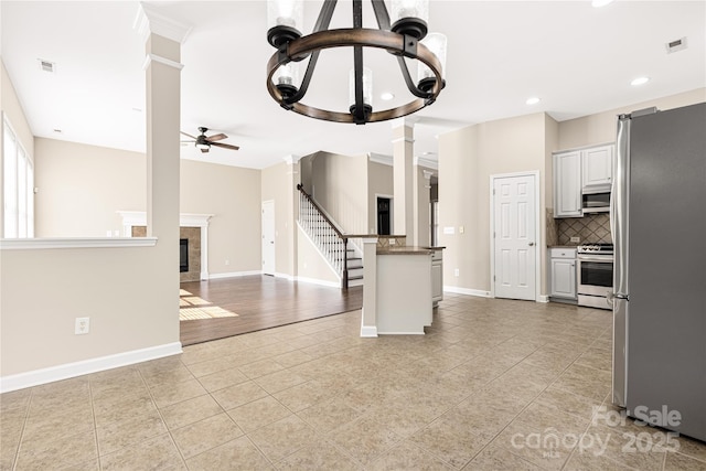 kitchen featuring ceiling fan, visible vents, appliances with stainless steel finishes, a glass covered fireplace, and decorative columns