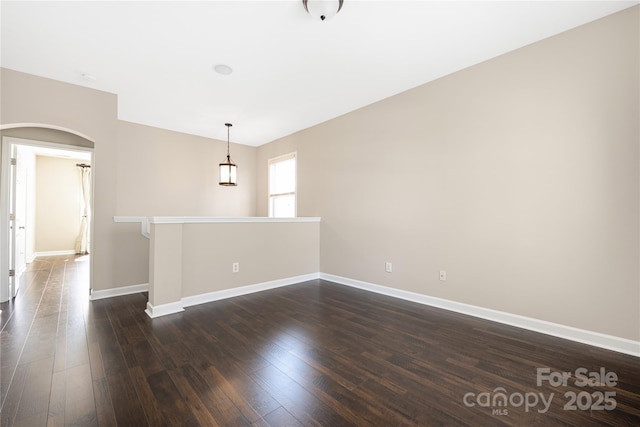 empty room featuring baseboards, arched walkways, and dark wood-type flooring