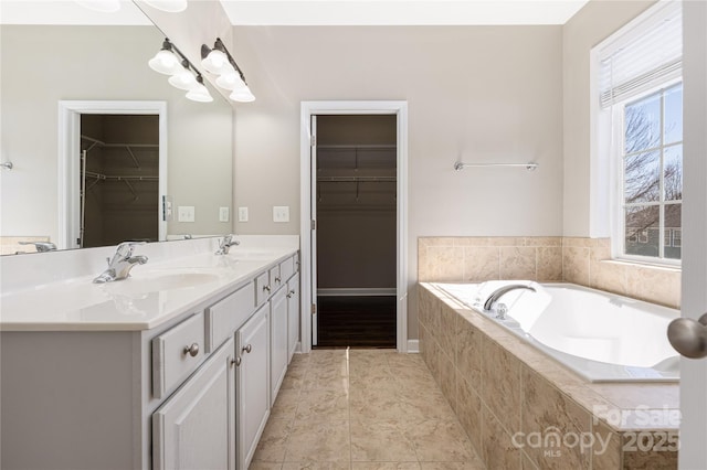 bathroom featuring a bath, double vanity, a sink, and a walk in closet