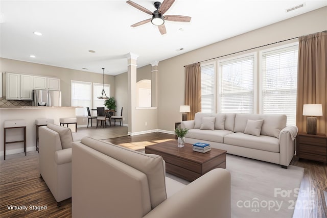 living area featuring a ceiling fan, a wealth of natural light, visible vents, and ornate columns