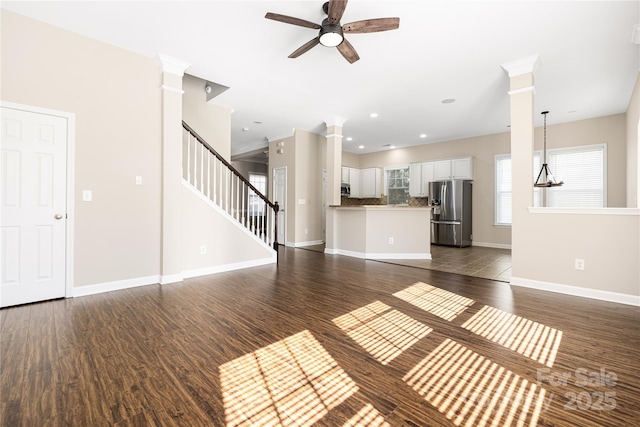 unfurnished living room featuring ornate columns, baseboards, dark wood-style floors, and ceiling fan with notable chandelier