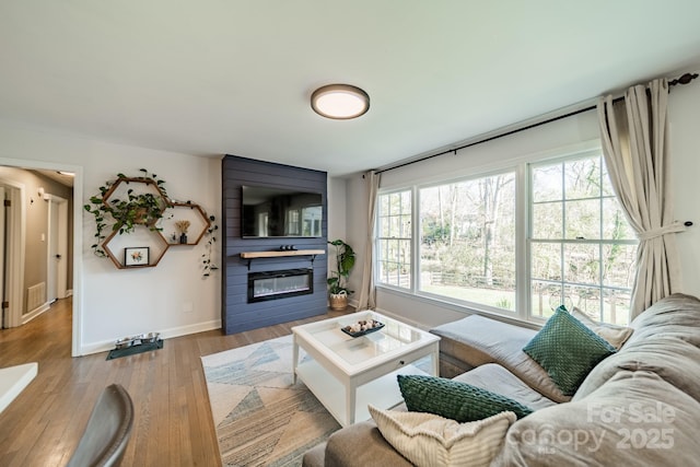 living area featuring a large fireplace, visible vents, baseboards, and wood finished floors