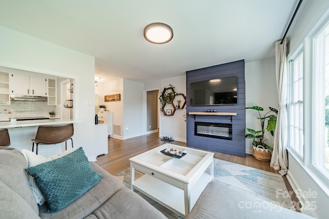 living area with a large fireplace, visible vents, baseboards, and wood finished floors