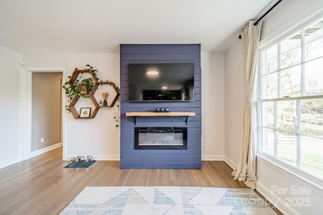 living area featuring a large fireplace, baseboards, and wood finished floors