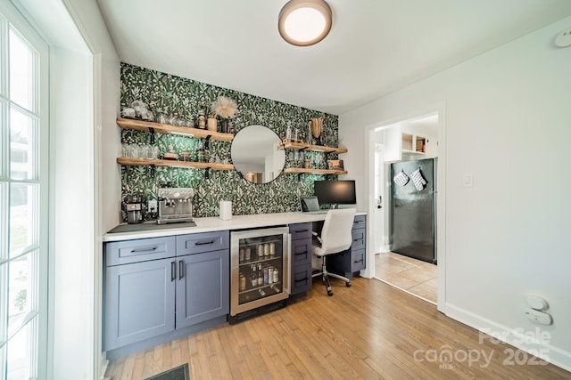 bar featuring wine cooler, tasteful backsplash, light wood-style flooring, freestanding refrigerator, and baseboards