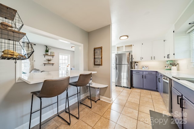 kitchen with a breakfast bar, light tile patterned floors, light countertops, gray cabinetry, and appliances with stainless steel finishes