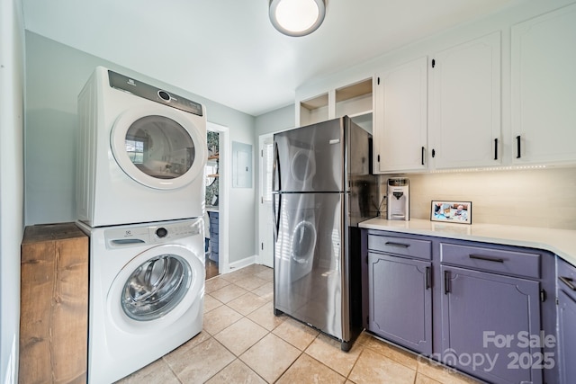 clothes washing area featuring light tile patterned floors, laundry area, and stacked washer / drying machine