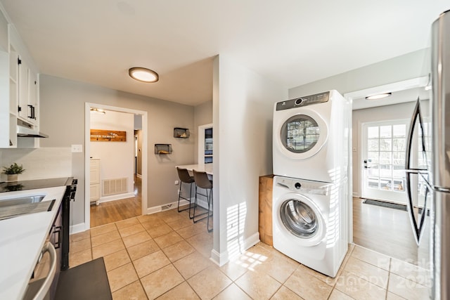 laundry area featuring stacked washer / drying machine, laundry area, visible vents, and light tile patterned flooring