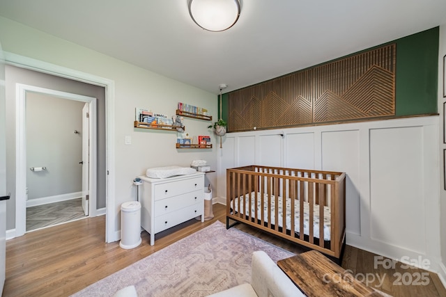 bedroom featuring a crib, baseboards, and wood finished floors