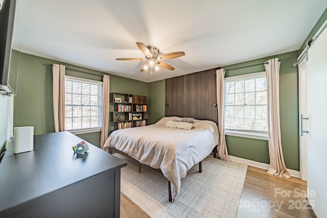 bedroom featuring light wood-style flooring, multiple windows, baseboards, and a ceiling fan