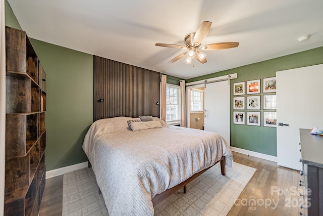 bedroom with ceiling fan, a barn door, wood finished floors, and baseboards