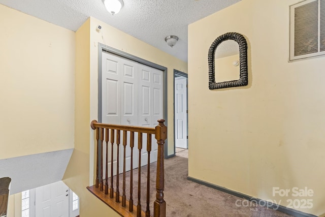 corridor with a textured ceiling, visible vents, carpet flooring, and an upstairs landing