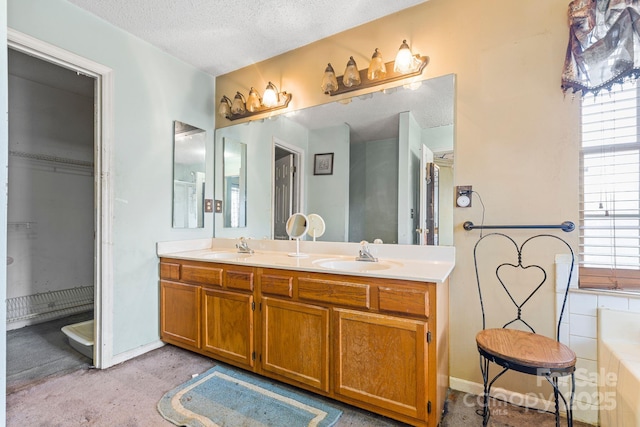 bathroom with double vanity, a textured ceiling, a washtub, and a sink