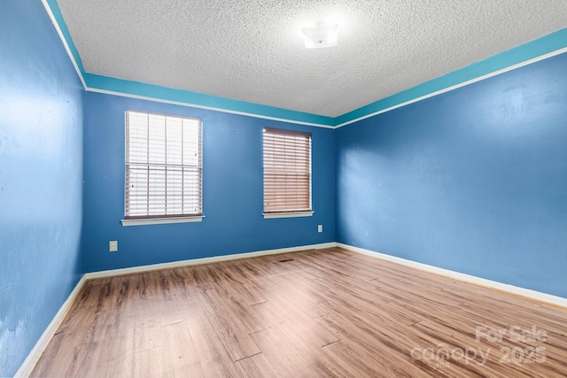 unfurnished room with a textured ceiling, baseboards, and wood finished floors