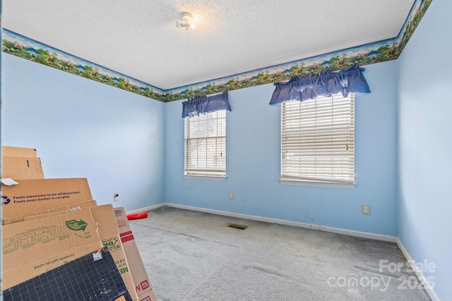 carpeted spare room with baseboards, visible vents, and a textured ceiling