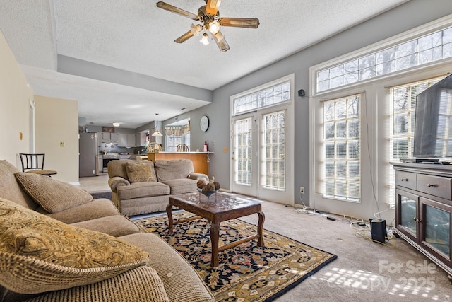 living area featuring baseboards, a ceiling fan, a textured ceiling, and light colored carpet