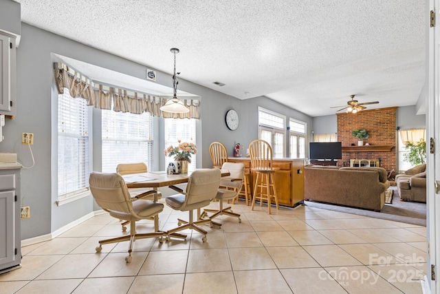 dining area with ceiling fan, a textured ceiling, light tile patterned flooring, and a fireplace