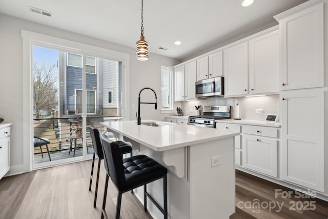 kitchen featuring a kitchen island with sink, stainless steel appliances, a sink, visible vents, and light countertops