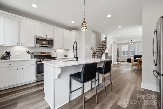 kitchen featuring wood finished floors, a sink, white cabinets, light countertops, and appliances with stainless steel finishes