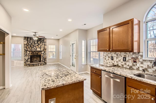 kitchen featuring light stone counters, a sink, stainless steel dishwasher, backsplash, and brown cabinetry