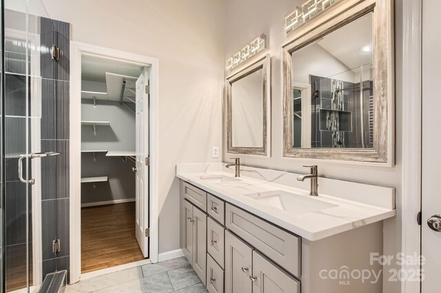 bathroom with double vanity, baseboards, an enclosed shower, and a sink