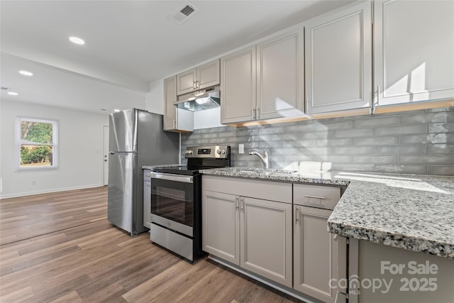 kitchen featuring visible vents, decorative backsplash, appliances with stainless steel finishes, light wood-style floors, and under cabinet range hood