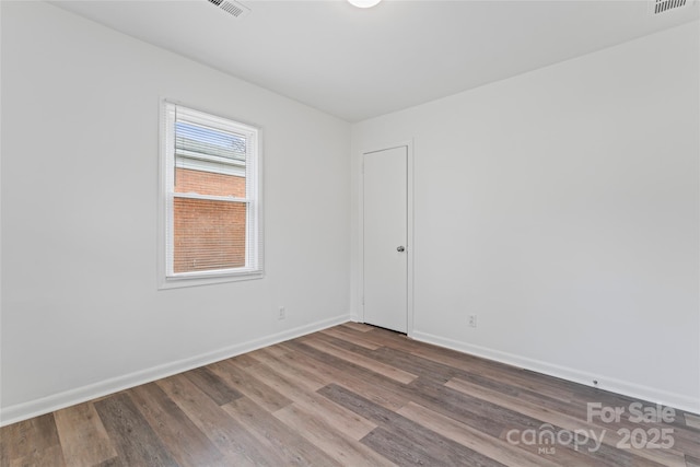 empty room with wood finished floors, visible vents, and baseboards