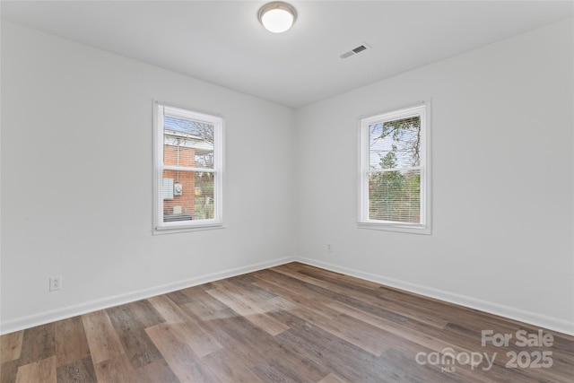 empty room with visible vents, wood finished floors, a wealth of natural light, and baseboards