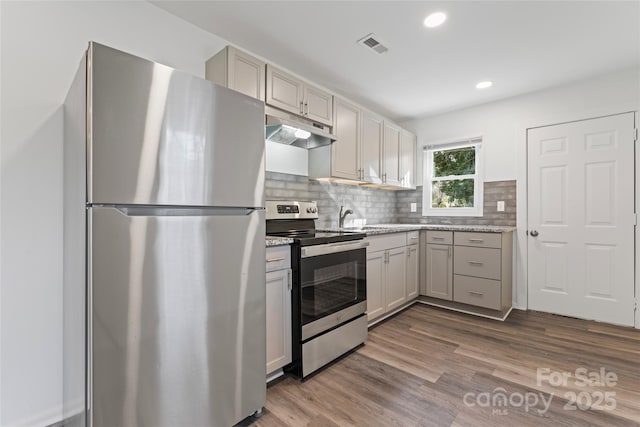 kitchen with under cabinet range hood, dark wood-style flooring, visible vents, appliances with stainless steel finishes, and backsplash