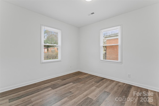 unfurnished room with a healthy amount of sunlight, visible vents, baseboards, and wood finished floors