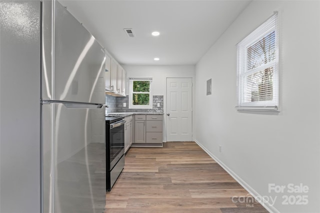 kitchen with visible vents, backsplash, appliances with stainless steel finishes, light wood-style floors, and baseboards