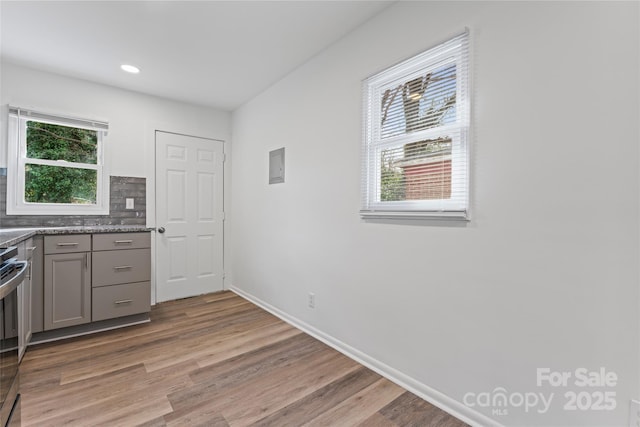 kitchen featuring tasteful backsplash, gray cabinets, light wood-style flooring, stainless steel range with electric cooktop, and baseboards