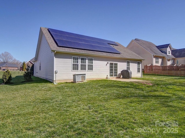 back of property with a yard, a patio area, fence, and roof mounted solar panels