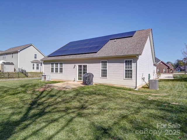 rear view of property with a shingled roof, central AC unit, a patio, a yard, and roof mounted solar panels